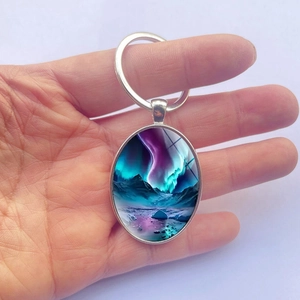 Oval silver metal keychain with aurora borealis mountain landscape held in hand
