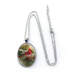 Oval silver cardinal bird necklace with winter pine branch artwork on white background
