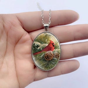 Oval cardinal bird pendant necklace with silver chain shown in hand presentation