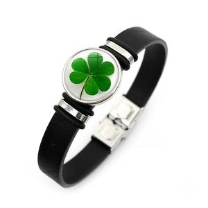 Detailed macro view of black leather bracelet with green four-leaf clover charm and snap clasp