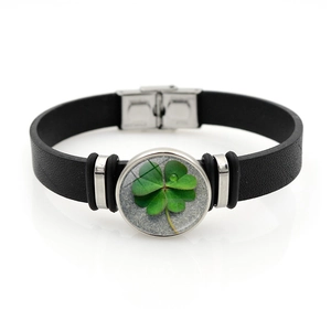 Detailed close-up of lucky four leaf clover charm on black leather bracelet with steel clasp