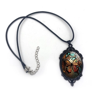 Vintage oval butterfly pendant necklace with black baroque filigree on a white background