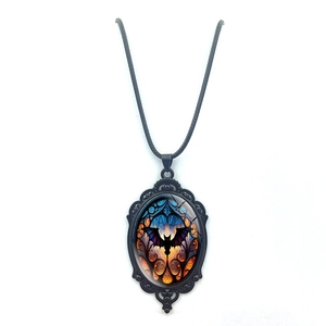 Close-up of gothic oval bat necklace featuring black filigree and orange-blue gradient pendant