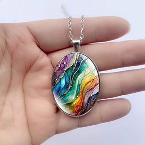 Oval pendant necklace with colorful abstract ripple art and silver chain held in hand