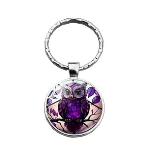 Close-up of glass owl keychain pendant with purple illustration on white background