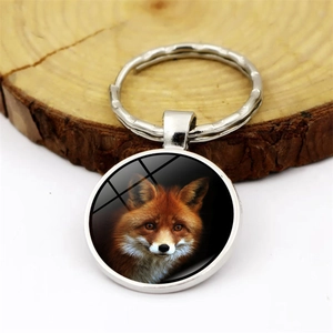 Silver metal keychain with round fox portrait glass pendant on wooden background