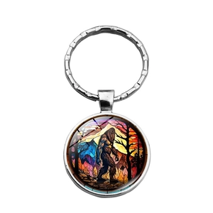 Close-up of Bigfoot glass cabochon keychain with vibrant sunset forest artwork