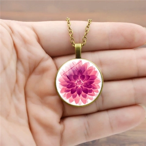 Vintage-Halskette aus Bronze mit einem runden Glasanhänger und pinker Dahlie in der Hand