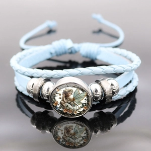 Makroaufnahme von blauem Vintage-Flechtarmband mit Engel-Fee-Anhänger und Metallperlen