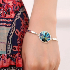 Close-up of a silver charm bracelet featuring a lighthouse art pendant worn on a wrist
