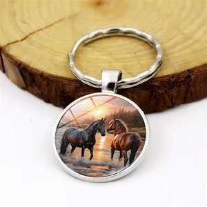Round metal keychain featuring sunset wild horses artwork on a rustic wood base