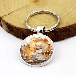 Exquisite silver angel keychain with round glass cabochon on a wooden tray