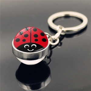 Cartoon ladybug keychain with red and black spotted pattern in a glass dome on black surface
