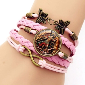Gros plan d'un bracelet rose tressé avec breloque Saint-Michel et symbole de l'infini