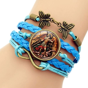 Détail d'un bracelet multicouche en cuir tressé bleu avec pendentif Saint Michel et symbole infini