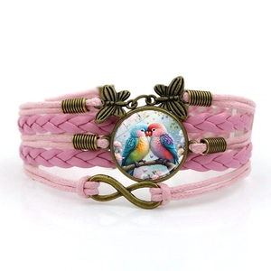 Détail du bracelet tressé rose avec gemme perroquet, symbole de l'infini et breloque papillon