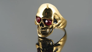 Macro detail of polished gold skull ring with striking red crystal eyes and vintage finish