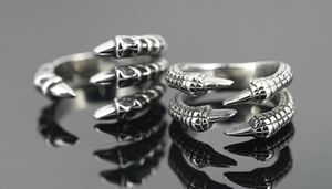 Detail view of retro dragon claw rings with punk scale texture on black mirror reflection