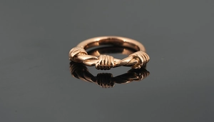 Detailed close-up of rose gold twisted rope ring with three knots on mirror surface
