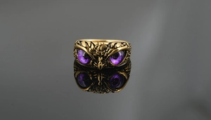 Detalle de un anillo de búho gótico dorado con ojos morados y relieve de plumas fino