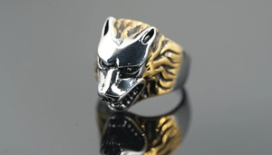 Macro detail of bicolour wolf head ring in silver and gold on reflective background