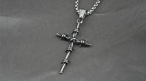 Macro detail of gothic cross pendant with barbed wire textures on textured fabric