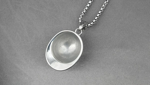 Detailed close-up of a vintage steel helmet pendant on a classic box chain necklace