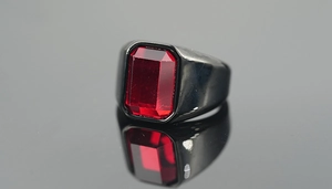 Macro shot of men's wide black ring featuring a large rectangular red gemstone and reflections