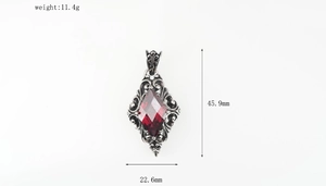 Macro detail of vintage titanium necklace pendant with red gem and intricate scroll patterns