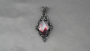 Macro shot of gothic rhombus pendant with a red gemstone and vintage hollow patterns