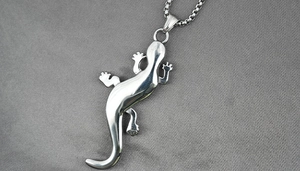 Close-up of polished titanium steel gecko pendant with minimalist box chain on grey fabric
