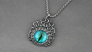 Macro del ciondolo a fiamma punk con occhio di drago blu e rune vintage su acciaio al titanio