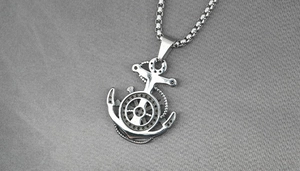 Macro detail of a vintage anchor pendant with a central helm on a steel box chain necklace