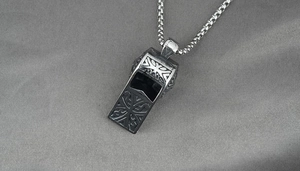 Detailed macro view of a vintage titanium steel cross whistle pendant with engraving