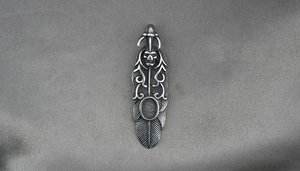 Détail d'un pendentif plume en acier titane avec motif de crâne et textures tribales