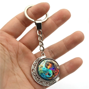 Handheld silver crescent moon keychain with a rotating yin yang nature landscape pendant