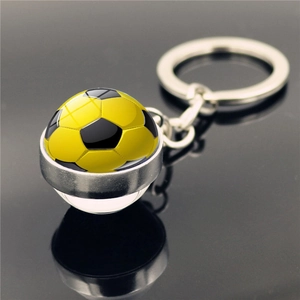 Close-up of a soccer pattern glass dome keychain with silver metal ring on reflective black surface