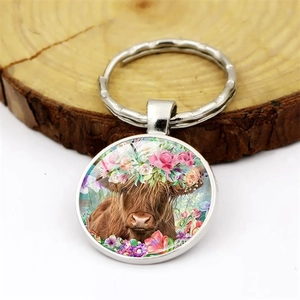 Silver Highland Cow keychain with floral crown glass dome pendant on wooden base