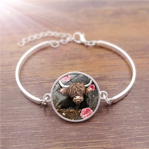 Detail of silver bracelet featuring a Scottish Highland Cow glass charm and pink flowers