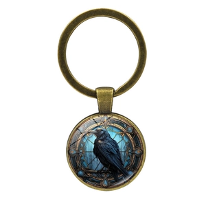 Detailed view of gothic crow illustration inside a round glass dome bronze keychain