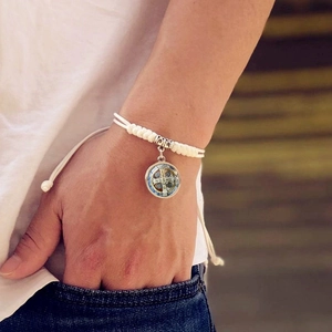 Dettaglio della medaglia di San Benedetto su un bracciale intrecciato bianco regolabile