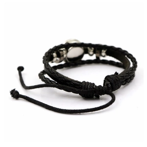 Dettaglio del bracciale multistrato in pelle intrecciata nera con disco in metallo e cordino