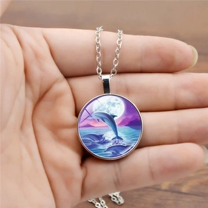 Detailed view of dolphin glass dome pendant necklace held in hand showing art pattern