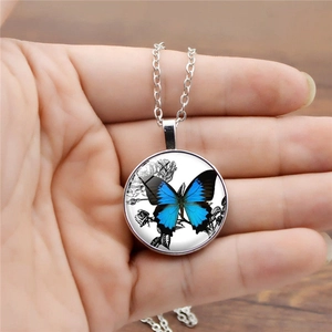 Detail of silver necklace with blue butterfly glass pendant held in hand over wood