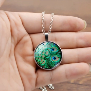 Detail of a silver peacock feather glass dome pendant necklace held in hand