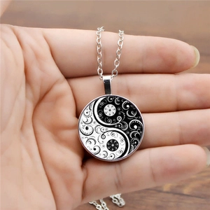 Détail du pendentif Yin Yang en argent avec des motifs volutes tenu dans la main