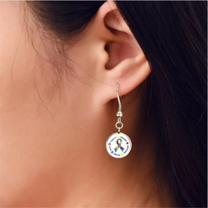 Vue rapprochée des boucles d'oreilles autisme en argent avec ruban puzzle et mots clés
