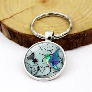 Hummingbird glass cabochon keychain with silver metal ring on a rustic wooden base