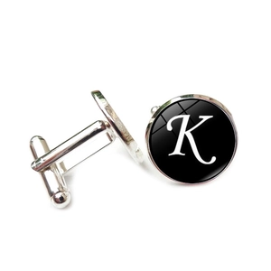 Detail of silver shirt cufflinks featuring a black glass dome with white letter K design