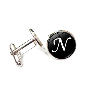 Detail view of silver cufflinks with black round inlay featuring white artistic letter N